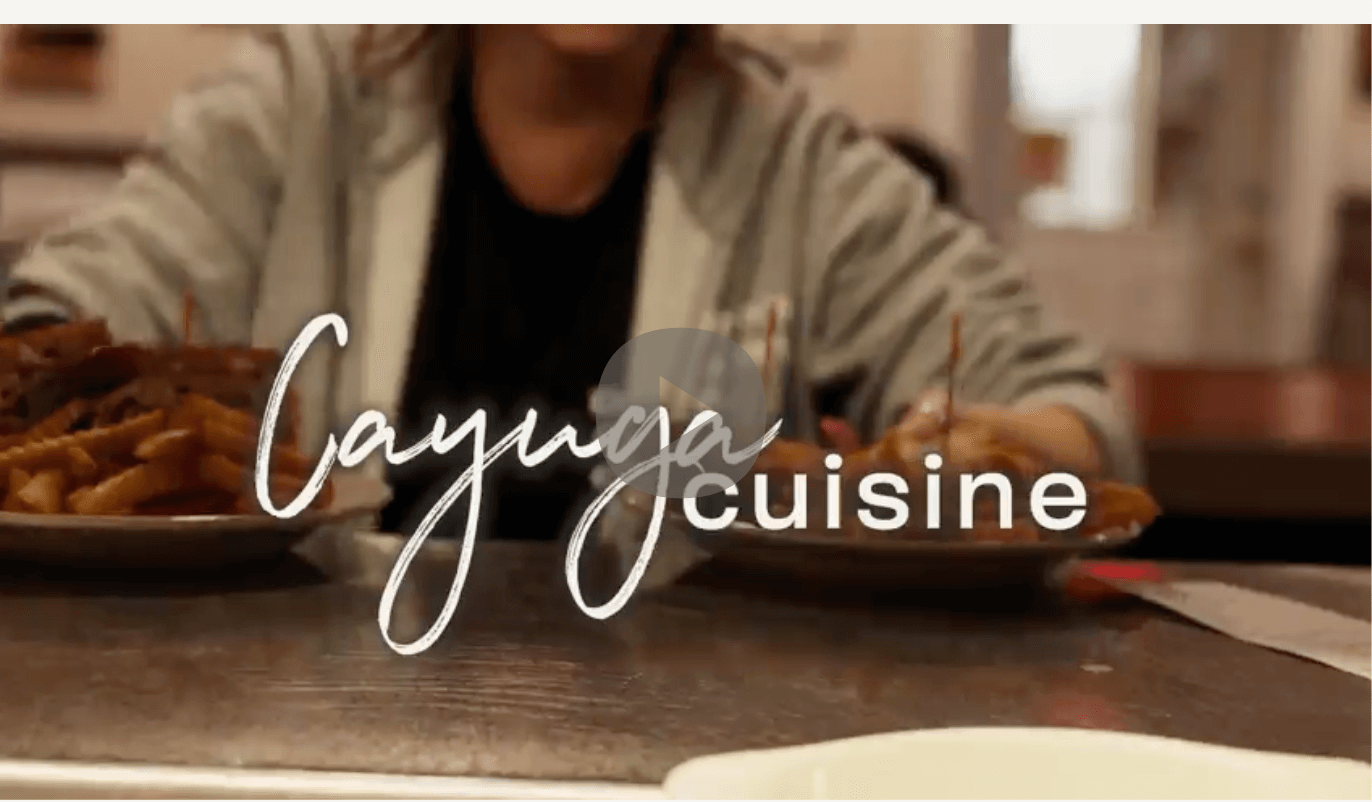 server with two plates of food with the overlay of the words Cayuga Cuisine